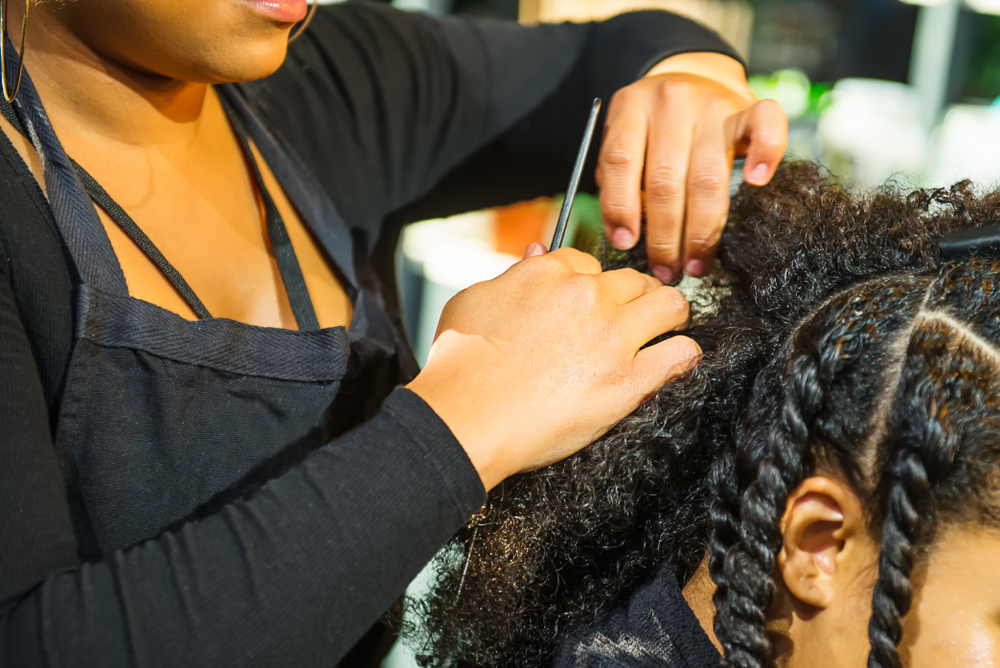 Close up african hairstylist braided hair of afro american female client in the barber salon. Black healthy hair culture and Style. Stylish therapy professional care concept. Selective focus