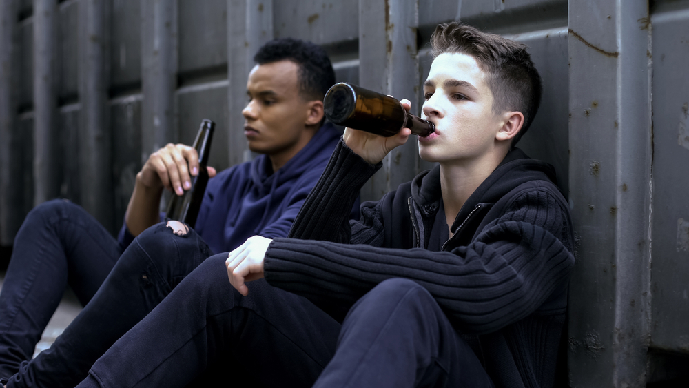 Teenager guys drinking beer sitting on road, bad company influence, experience