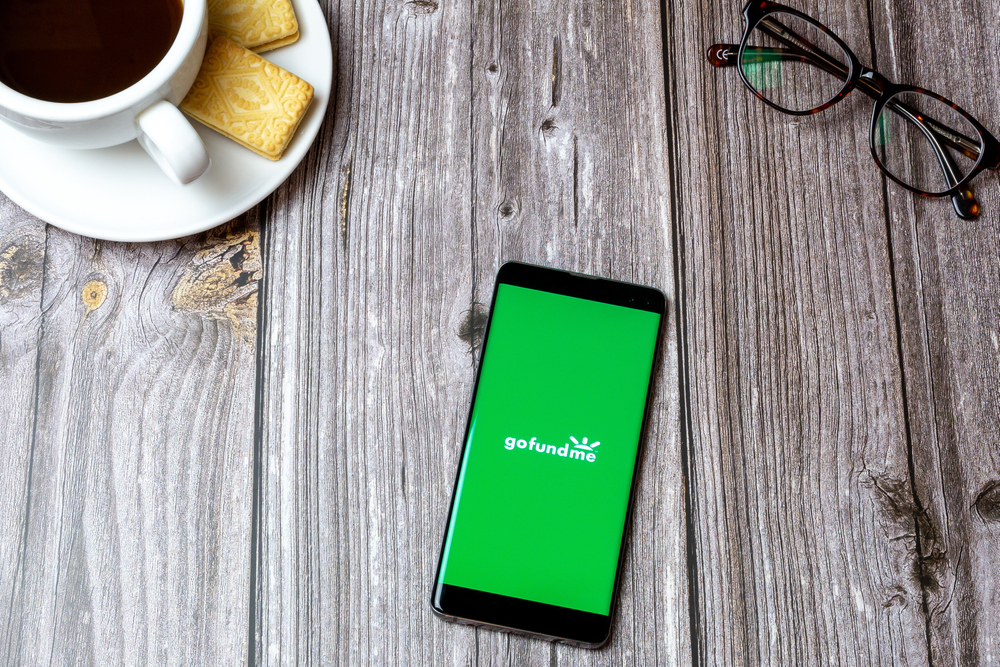 02-24-2021 Portsmouth, Hampshire, UK A mobile phone or cell phone on a wooden table with the Gofundme app open next to a coffee and glasses
