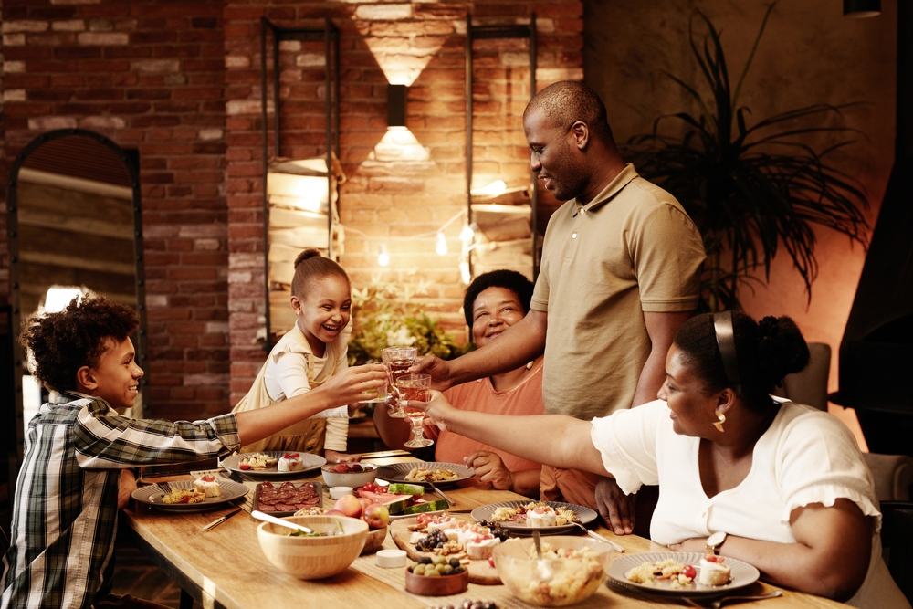Warm toned portrait of happy African-American family clinking glasses and toasting while enjoying dinner together at evening