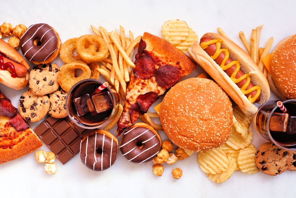 Junk food table scene scattered over a white marble background. Collection of take out and fast foods. Pizza, hamburgers, french fries, chips, hot dogs, sweets. Top view.