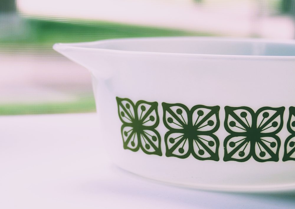 Vintage milk glass casserole dish. It is white with green flower pattern. It is in front of a window.