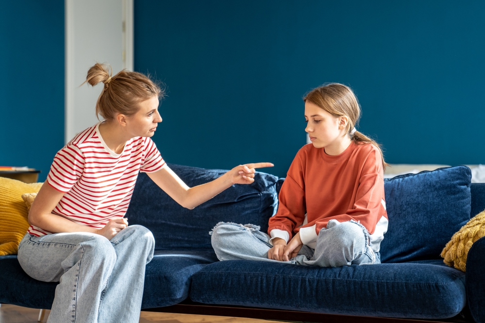 Angry mother pointing upset child sitting on sofa in living room. Conflict children and parents.Toxic mom humiliates young girl for bad behavior. Difficulties in raising teenage daughter