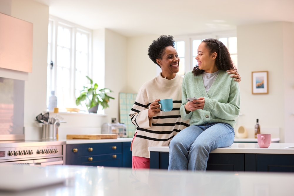 Mother Talking With Teenage Daughter At Home As She Checks Social Media On Mobile Phone