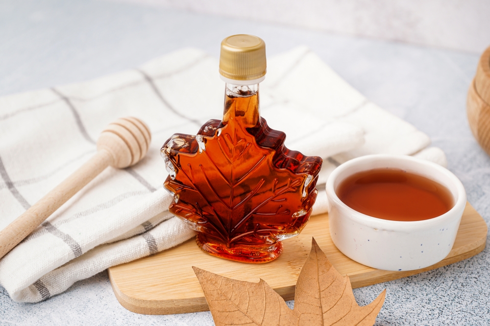 Bottle and bowl of tasty maple syrup on table
