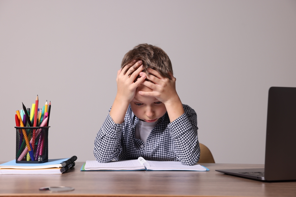 Little boy with stationery suffering from dyslexia at wooden table