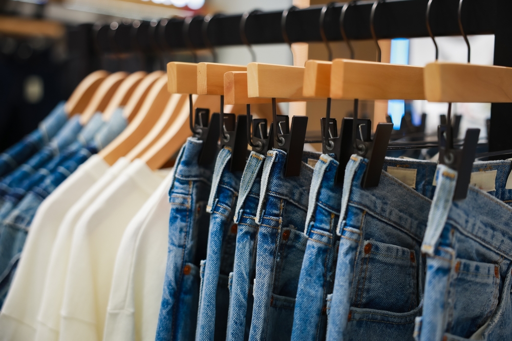 Jeans on the hanger in the store. Clothes on hangers in shop for sale. Blur background. Fashionable clothes in a boutique. Various clothing on market. Shopping in store.
