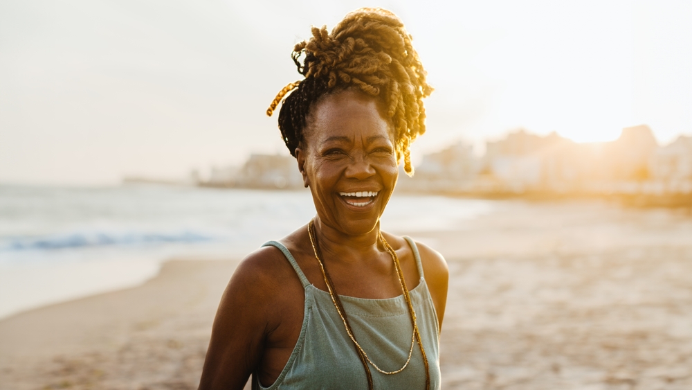 Joyful senior African American woman with braids enjoying a beautiful sunset at the beach, exuding happiness and confidence.