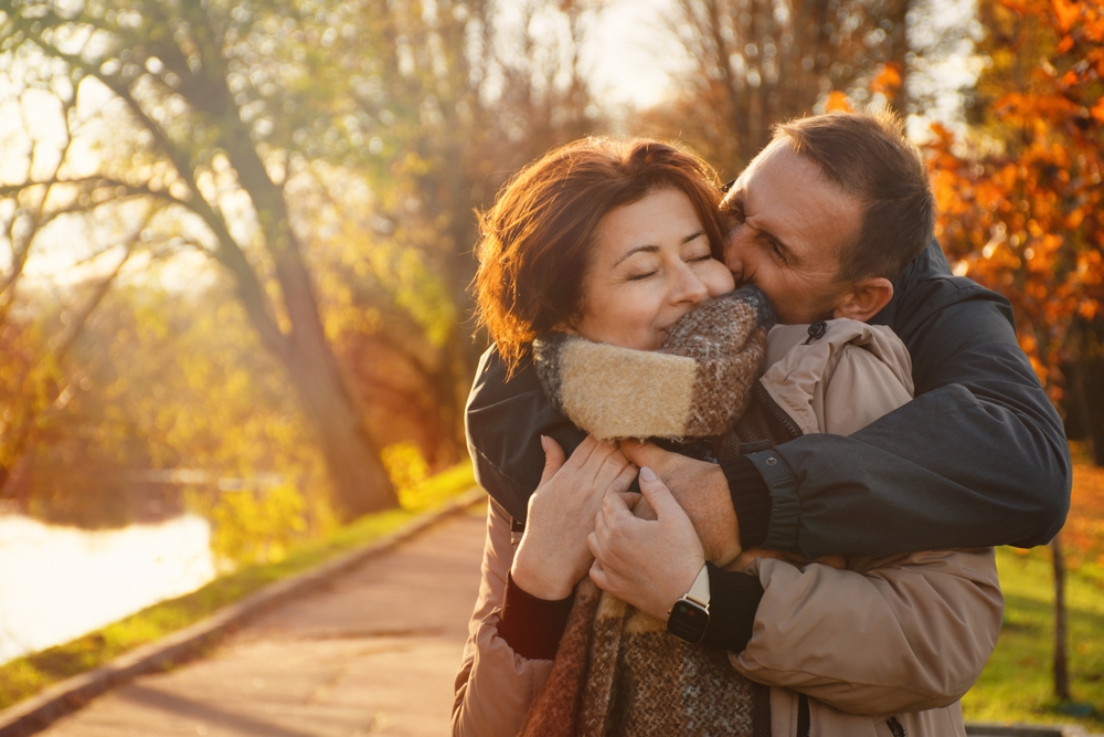 happy married couple over 50 years old, walking in the park in autumn on a warm sunny day, hugging, spending a day off together.
