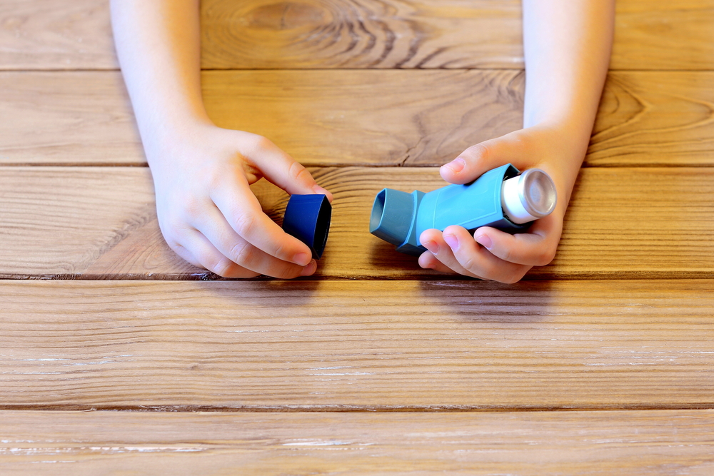 Small child holds asthma inhaler in his hands. Inhalation treatment of respiratory diseases. Allergy and bronchial asthma concept. Old wooden background