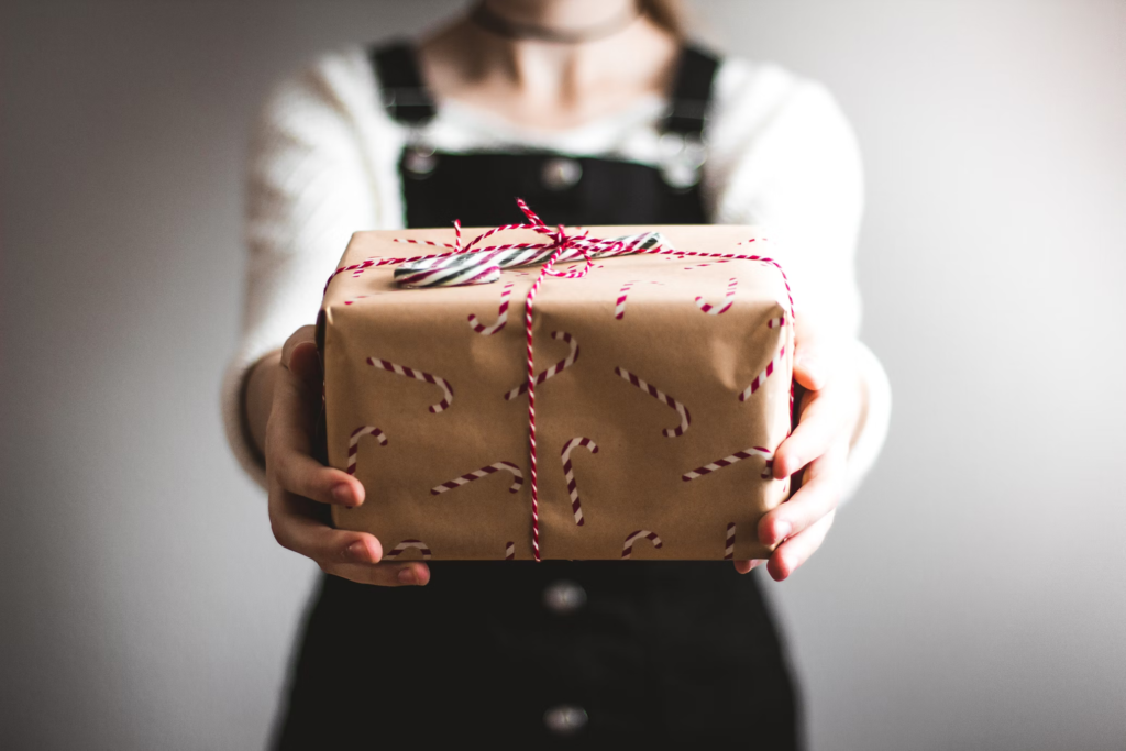 Person holding a brown gift box wrapped with red and white string, representing unwanted gifts that clutter closets.