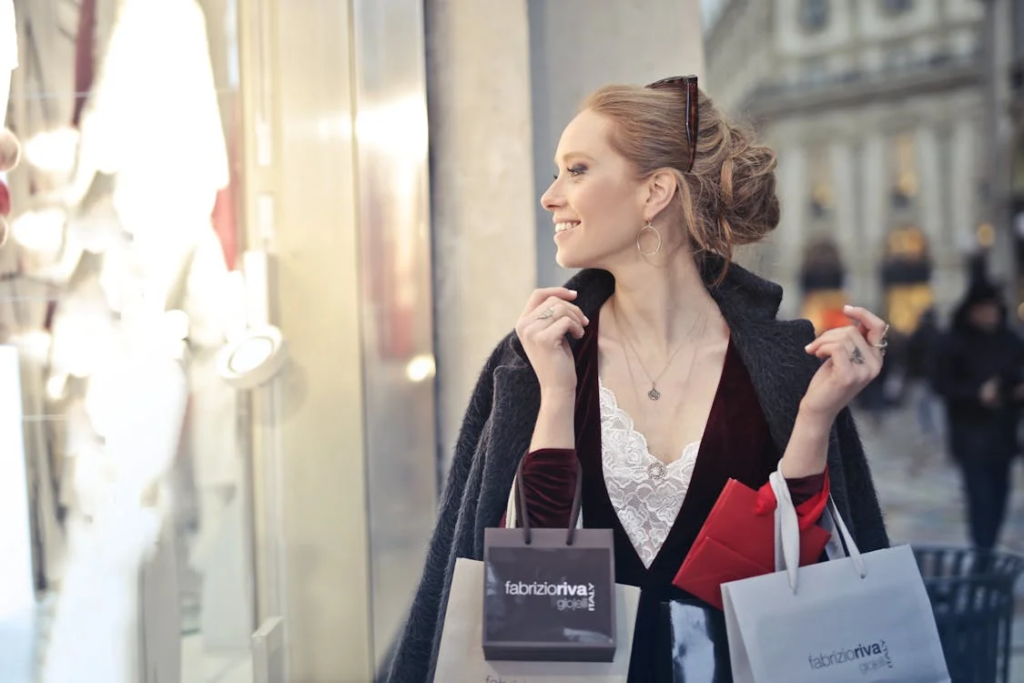 Smiling woman shopping with multiple branded shopping bags, looking at store windows, representing impulse buying habits.