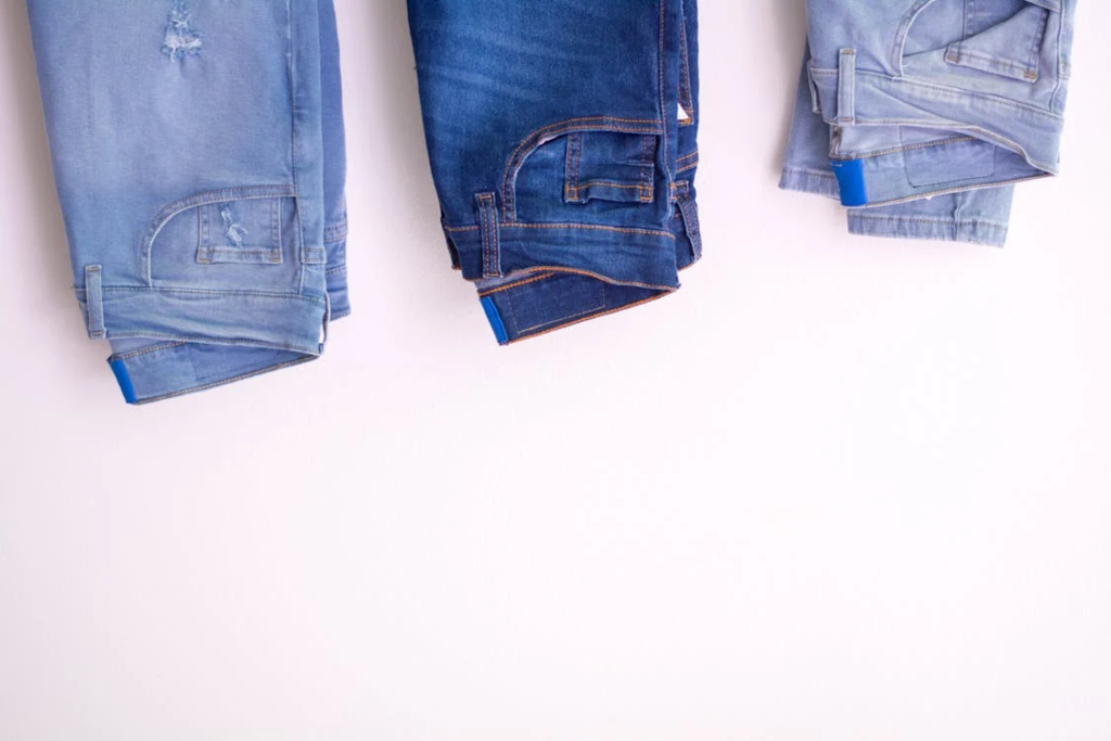 Three pairs of folded jeans in different shades of blue laid out on a white background, symbolizing clothes that may no longer fit.