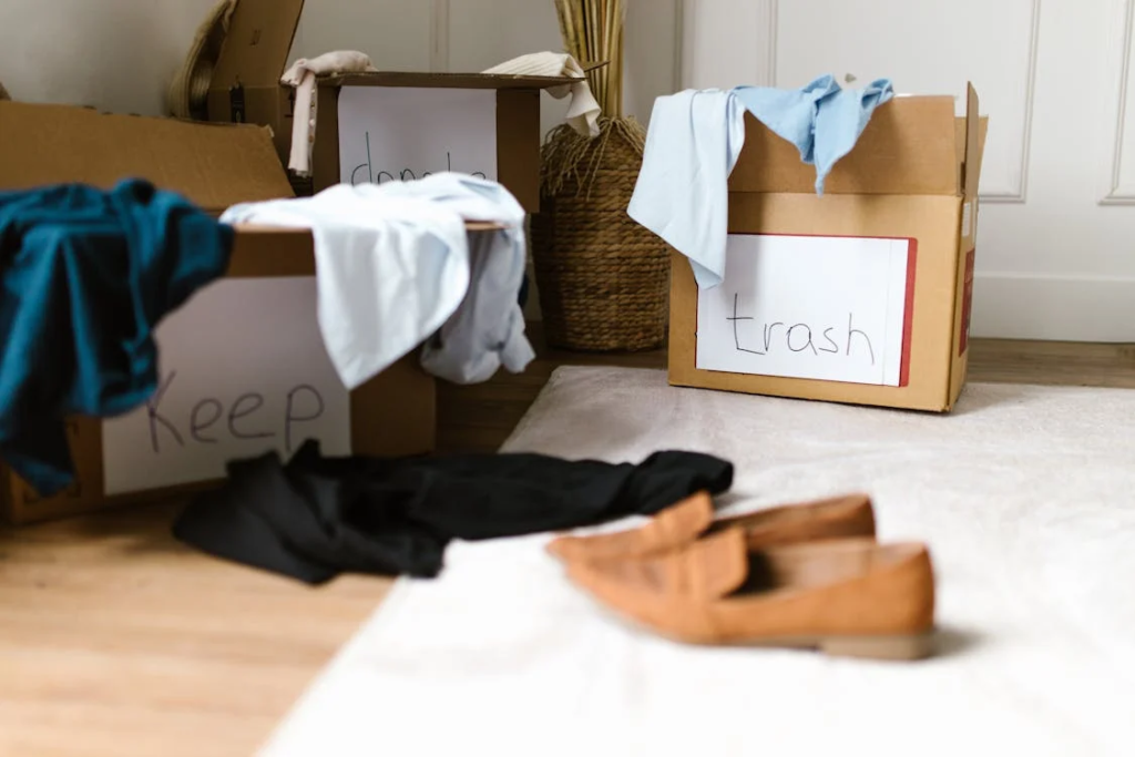 Cardboard boxes labeled 'Keep' and 'Trash' with clothing items sorted into each, and shoes on the floor, demonstrating an organized decluttering process.