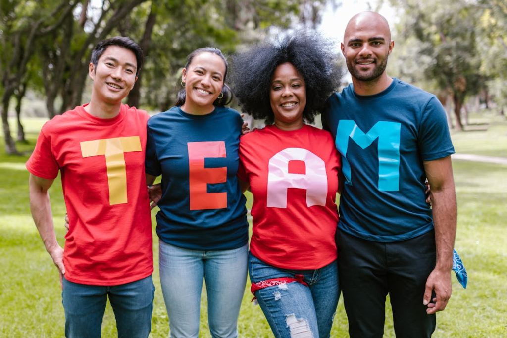 Four diverse people standing together outdoors wearing t-shirts that spell out 'TEAM' in red and blue, representing promotional t-shirts that accumulate over time.