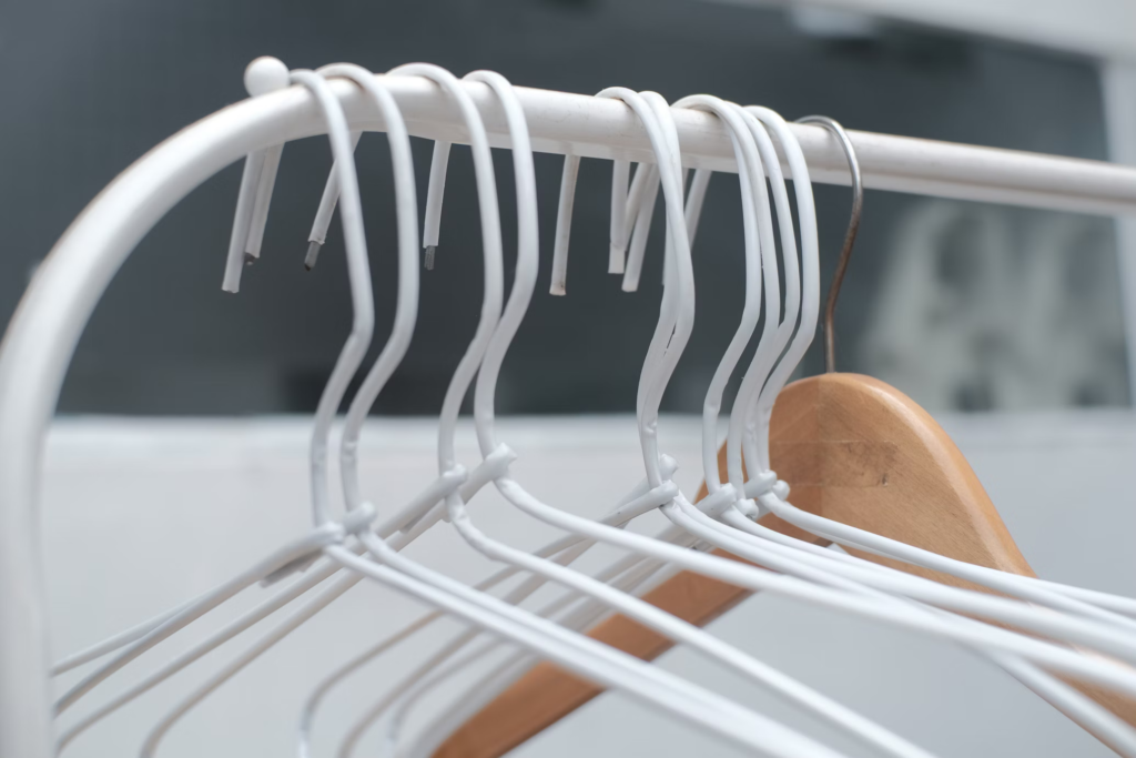 Close-up of several white wire hangers with one wooden hanger, illustrating the contrast between poor quality and premium closet hangers.