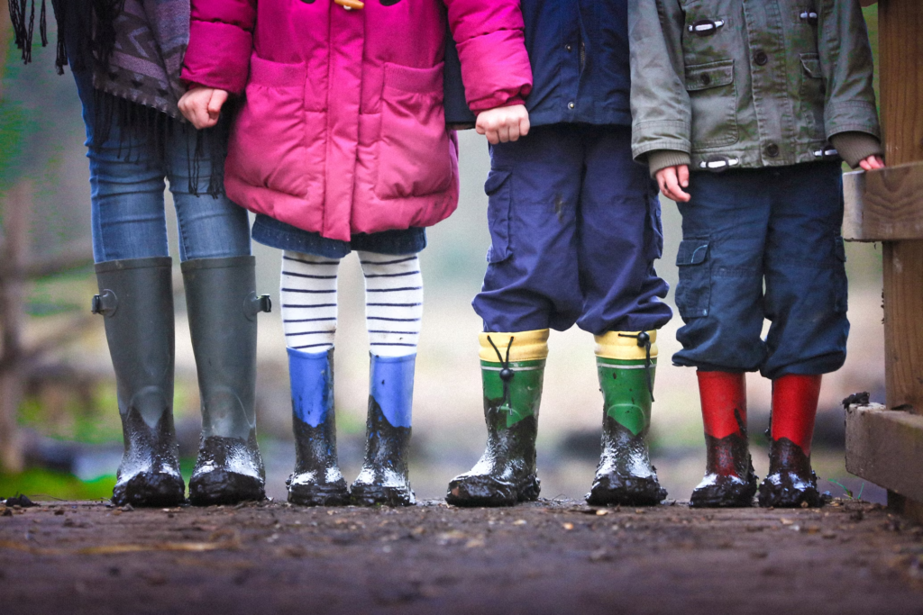 Four pairs of muddy children's rain boots standing in a row, symbolizing the forgotten children like the 6-year-old girl in Deltona who was abandoned by her mother and boyfriend.