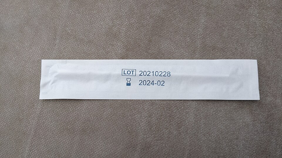 A white paper sleeve for a DNA testing sample with a lot number 20210228 and an expiration date of 2024-02. The sleeve appears to be for storing or submitting a paternity test sample, placed on a neutral gray background.