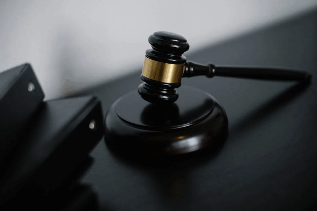 A wooden judge's gavel with a gold band resting on its sound block against a dark surface. The image, shot from above in low-key lighting, symbolizes legal proceedings and justice, relevant to lawsuits against DNA testing companies.
