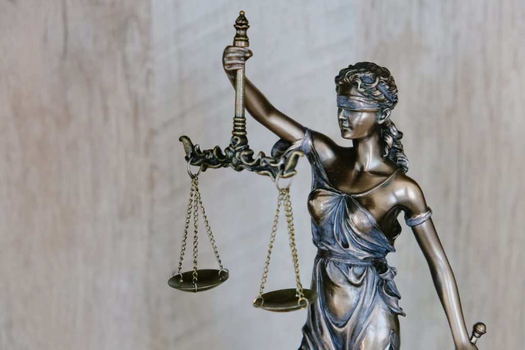 Bronze statue of Lady Justice (Justitia) holding balanced scales in one hand and a sword in the other, with a blindfold covering her eyes, symbolizing impartial judgment in the legal system.