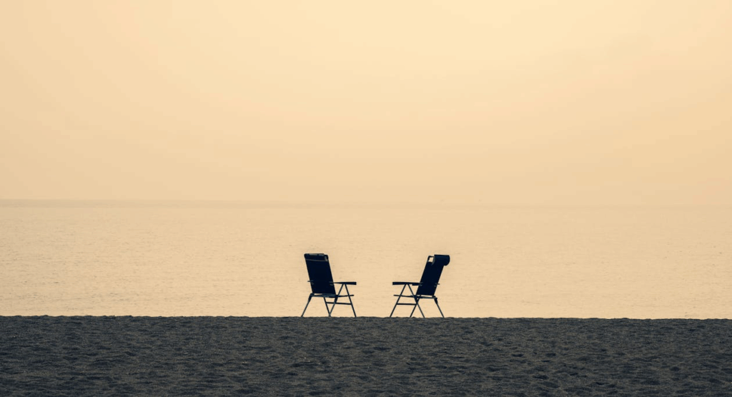 Two empty beach chairs facing the ocean at sunset on a deserted shoreline, symbolizing the abandoned recreational spaces as residents avoid the beach due to inappropriate behavior.