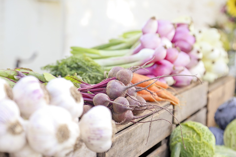 Assortment of fresh vegetables including beets, carrots, and radishes displayed in wooden crates at a farmers market.
