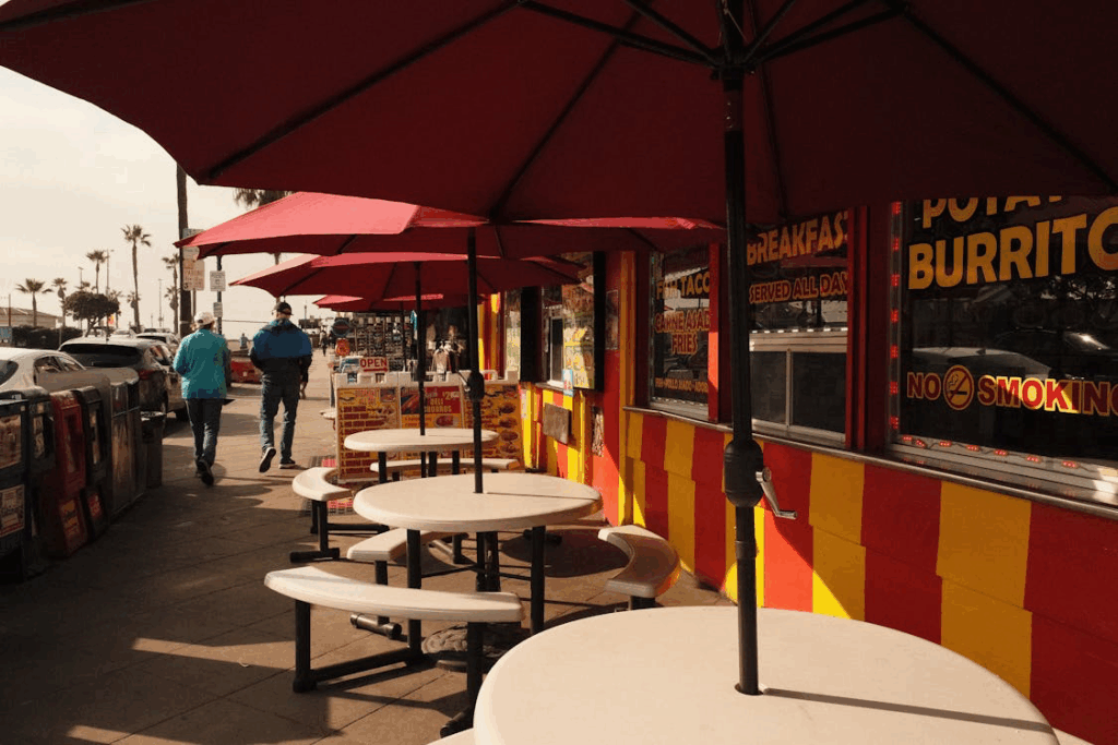 Colorful burrito stand with red and yellow striped exterior and outdoor seating under red umbrellas, offering an alternative to home cooking as grocery prices rise.