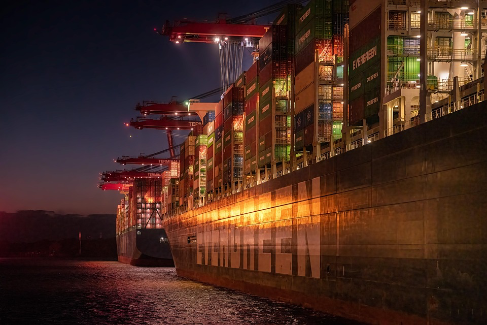 Large cargo container ship loaded with shipping containers illuminated at night, representing the global supply chain that influences regional food costs.