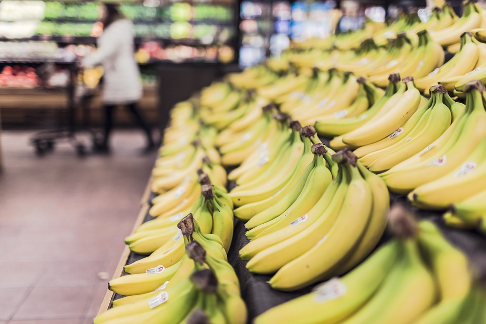 Fresh yellow bananas displayed in a grocery store produce section with blurred shopping area in the background.