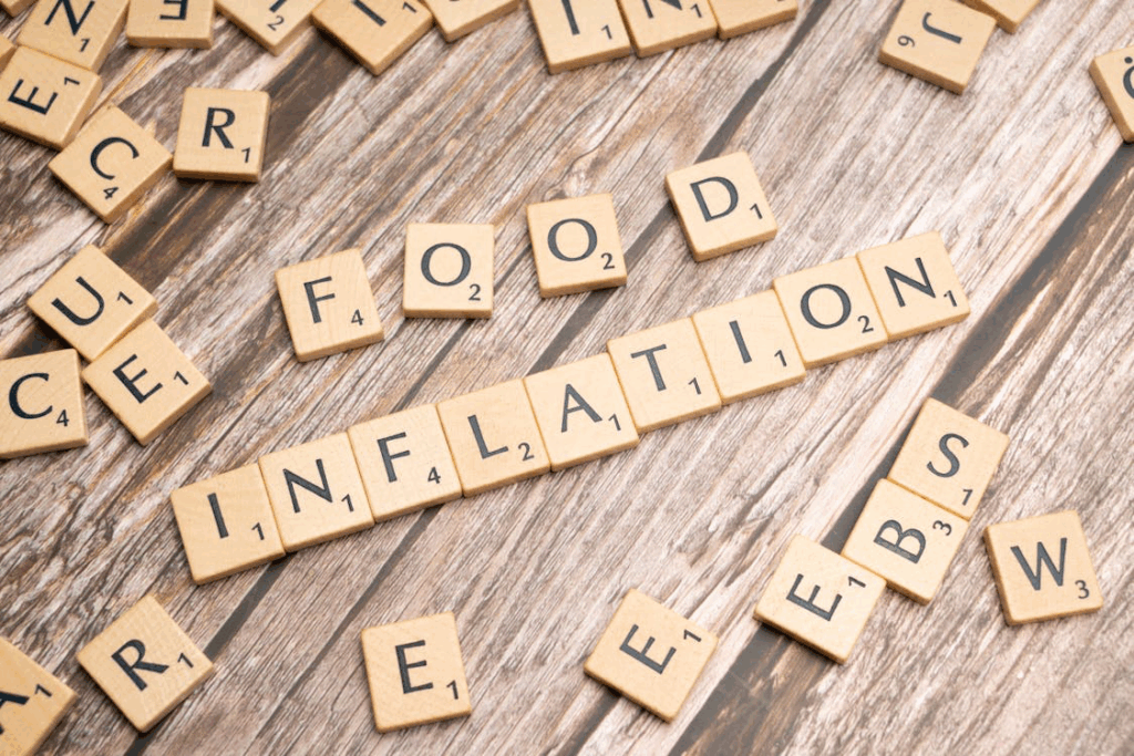 Wooden Scrabble tiles spelling out 'INFLATION' and 'FOOD' on a rustic wooden surface, illustrating the rising grocery prices affecting households across America.