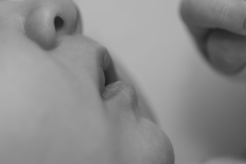 Close-up, black and white image of an infant's mouth and facial features. The intimate perspective shows the delicate skin and gums where teething pain occurs. This clinical portrayal illustrates the vulnerable area where some parents mistakenly apply alcohol for pain relief, not realizing the potential dangers of absorption through oral tissues.