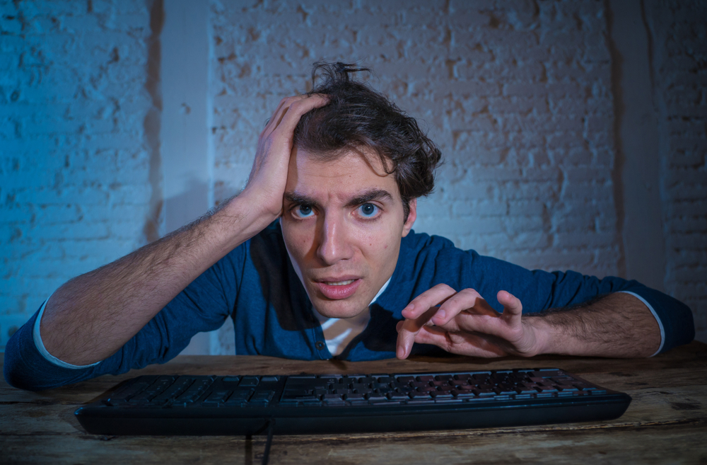 Addict young man alone at night on computer laptop working, online gambling, watching porn or playing games late at home or using the internet chat social media network. In technology addiction.
