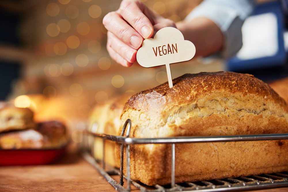 Sales Assistant In Bakery Putting Vegan Label Into Freshly Baked Baked Sourdough Loaves Of Bread