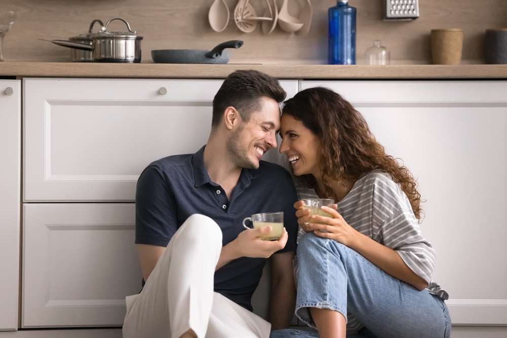 Hispanic couple sit on warm floor with mugs in cozy kitchen, enjoy romantic dating, house-warming, pleasant talk and beverage, spend relocation day to new own house. Cohabitation, relationships, love