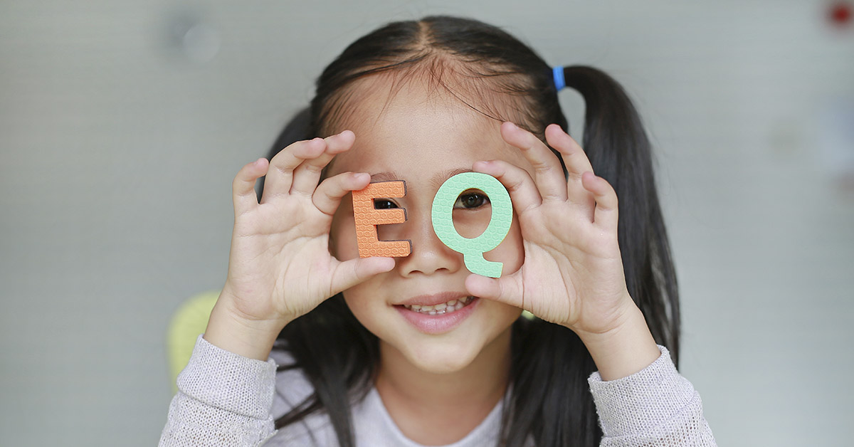 Child holding letters E and Q up to their face. Child Emotionally Intelligence concept