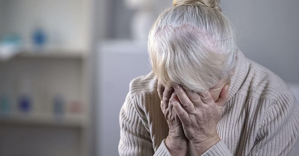 elderly woman crying with face in palms