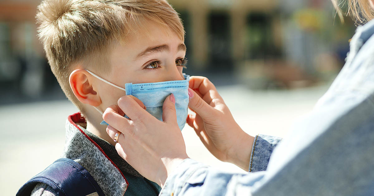 parent putting a surgical style mask on a child. Pandemic / COVID-19 concept