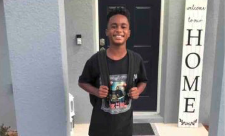 Eleven-year-old Louis Johnson III smiles brightly at his front door, wearing a black t-shirt and backpack, standing beside a "welcome to our HOME" sign. This heartbreaking glimpse shows the vibrant boy his parents described as someone who "would light up any room with his infectious smile.
