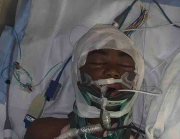 LJ lies unconscious in a hospital bed, surrounded by medical equipment, with breathing tubes and bandages covering his head as he fought for his life for two days following the incident that occurred while his father briefly stepped outside.