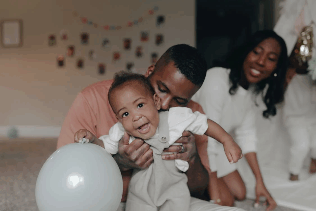 A family moment showing parents with their baby who has a white balloon nearby, illustrating how balloons are common at family celebrations, making awareness about helium-related death prevention crucial for protecting vulnerable children.