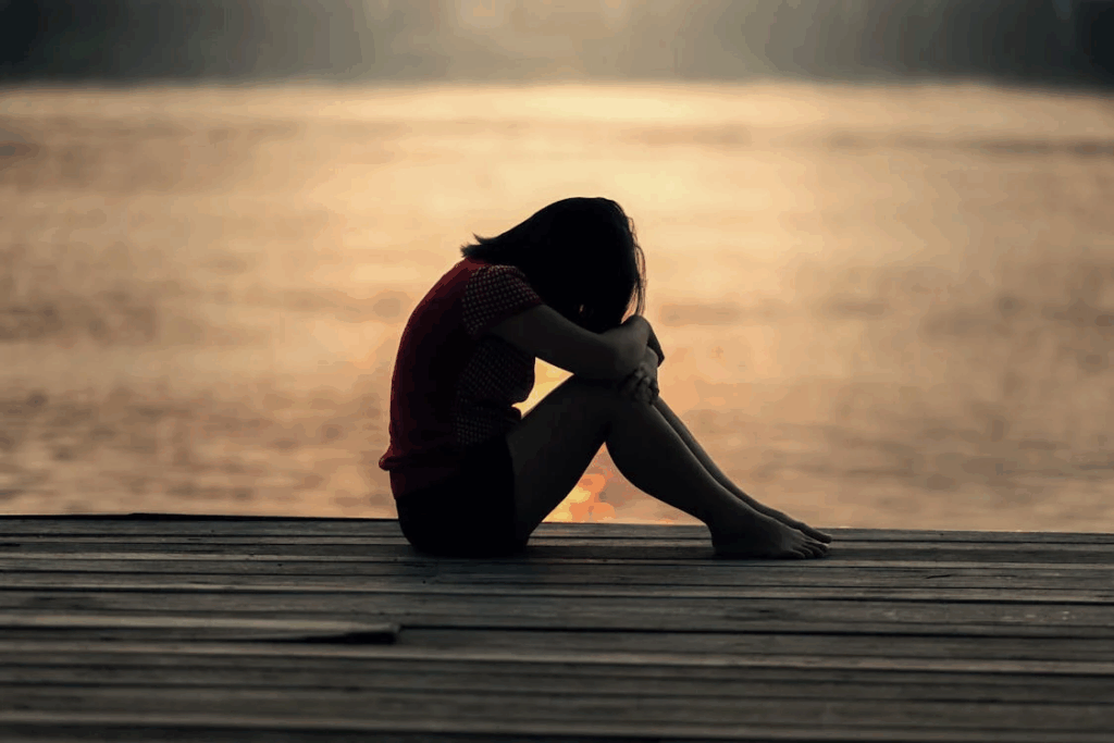 A person sitting alone on a dock at sunset, shoulders hunched and head down, symbolizing isolation and sadness often experienced in the early stages of abusive relationships.
