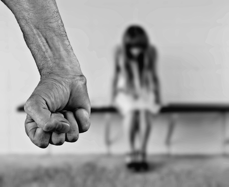 A clenched fist in the foreground with a blurred figure in the background, illustrating the power imbalance and threat of violence.