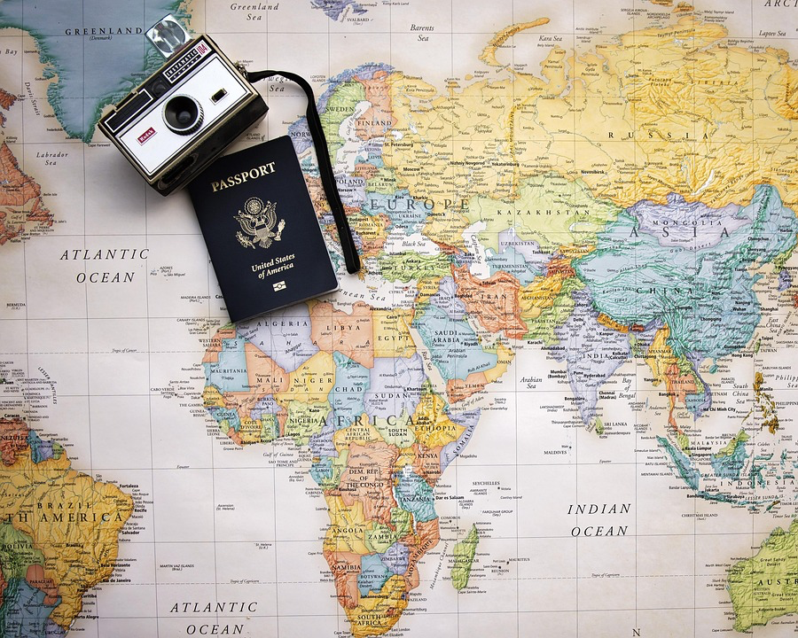 A passport, camera, and map spread across a world map, representing the essential items and planning needed when preparing to leave an abusive situation.