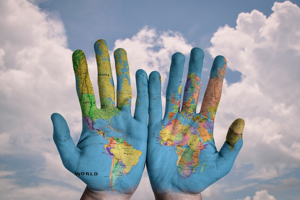 Hands painted as a world map held up against a blue sky with clouds, symbolizing the global support networks available for domestic abuse survivors worldwide.
