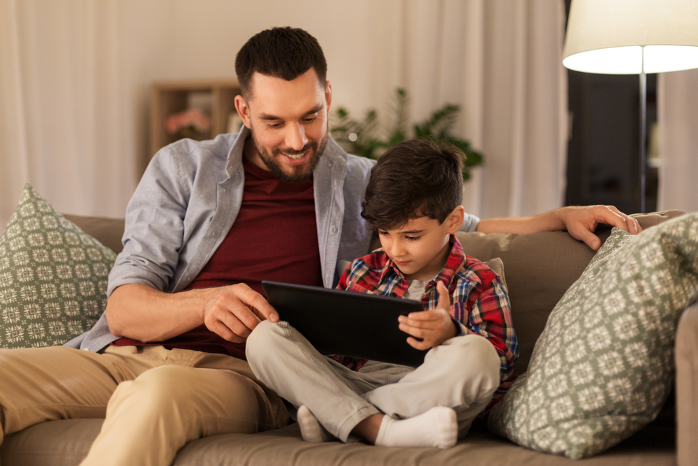 family, fatherhood, technology and people concept - happy father and little son with tablet pc computer sitting on sofa at home