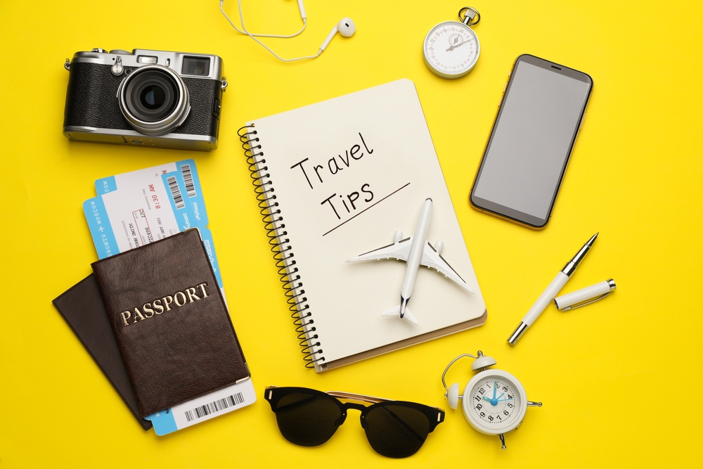 Flat lay composition with phrase Travel Tips written in notebook, passports, tickets and toy airplane on yellow background