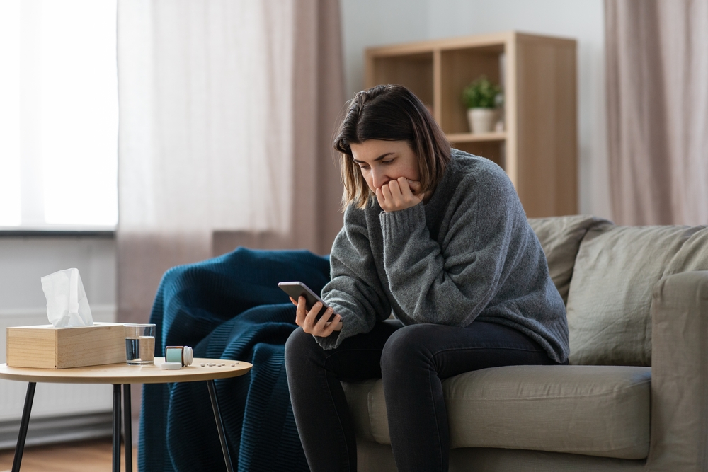 mental health, psychological help and depression concept - stressed woman with medicine pills on table holding smartphone at home