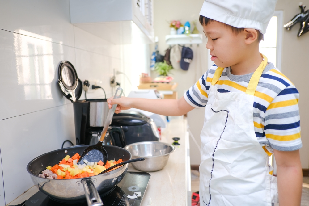 Cute happy smiling Asian 8 years old boy child wearing chef hat and apron having fun preparing, cooking healthy Homemade Japanese Curry Rice at home, Little home helper, EF skill development concept