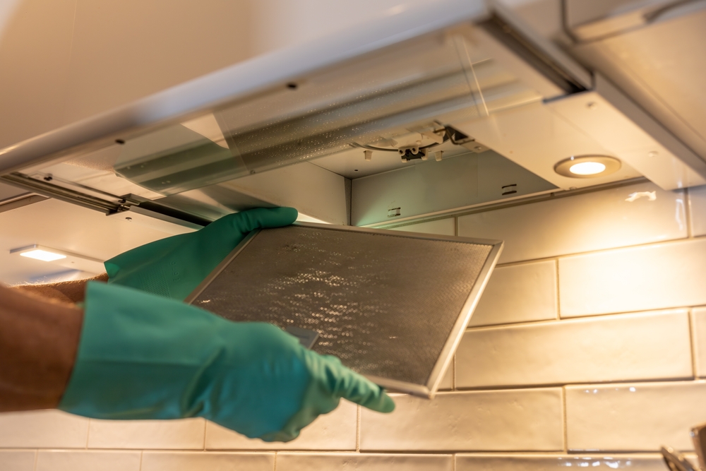 A person with rubber gloves removes an airfilter above a stove top for cleaning.