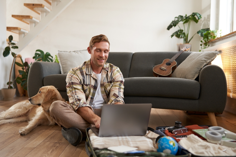 Home Relax. Handsome Indian Guy Sitting On Couch And Switching Tv Channels, Smiling Young Eastern Man Holding Remote Controller, Relaxing On Comfortable Sofa In Living Room, Copy Space